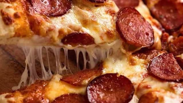 Cheesy pizza slice topped with pepperoni, with gooey cheese stretching from the crust.