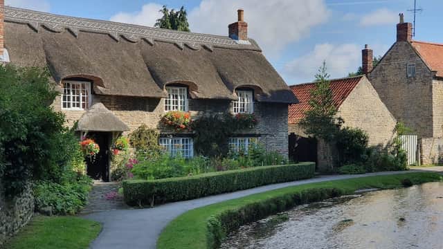 Thatched cottage with flower boxes, lush greenery, and a tranquil stream in Thornton-le-Dale, Yorkshire.