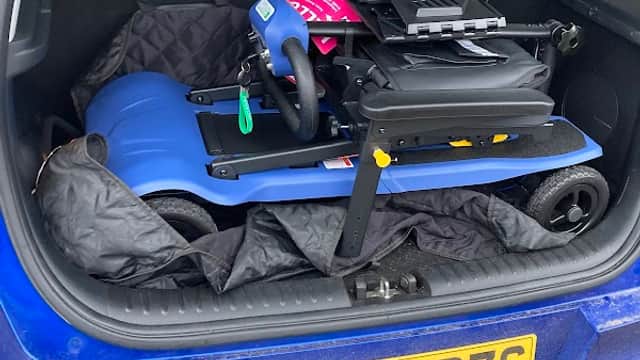 Blue vehicle trunk with a compact mobility scooter secured and covered in a quilted blanket.