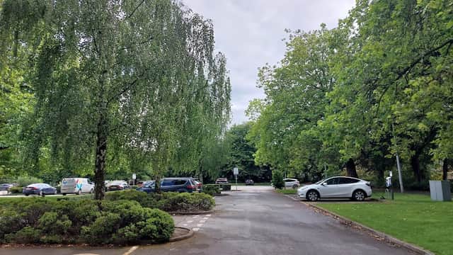 Pay & Display car park at Clifton Park Museum, lined with trees and shrubs, featuring parked cars and a cloudy sky.