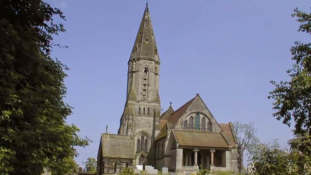 Historic stone church with a tall spire, surrounded by trees and a clear blue sky in East Heslerton, Yorkshire.
