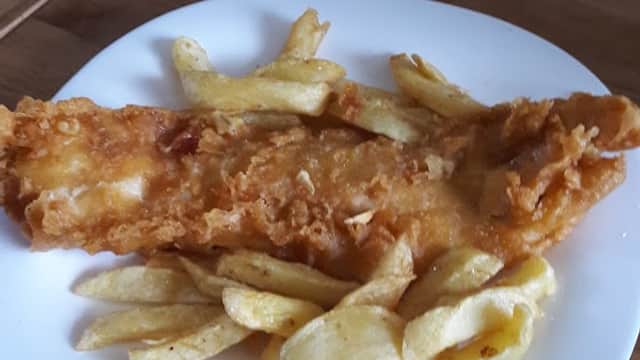 Crispy battered fish fillet served with golden fried chips on a white plate.