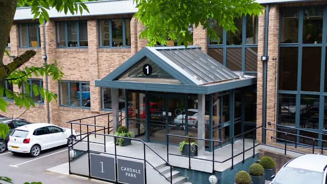 Modern brick building with a glass entrance, surrounded by greenery and parked cars, labeled "1 Cardale Park."