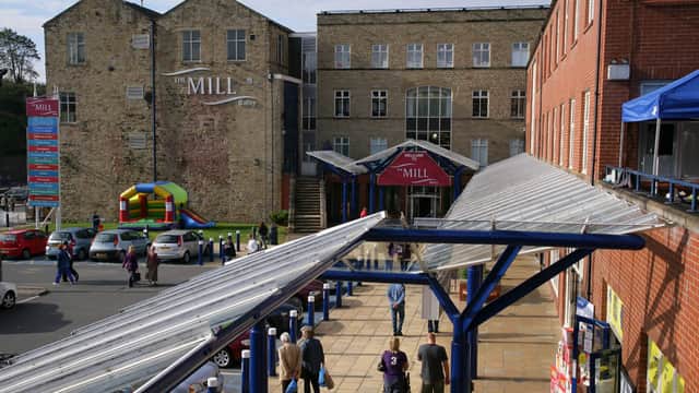 Shoppers walking under a glass canopy towards a large brick factory outlet, with a stone building and a bouncy castle nearby.
