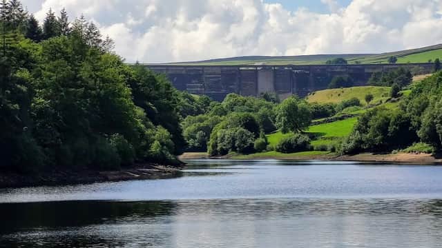 Ryburn Reservoir with lush greenery, calm water, and a dam in the background under a partly cloudy sky.