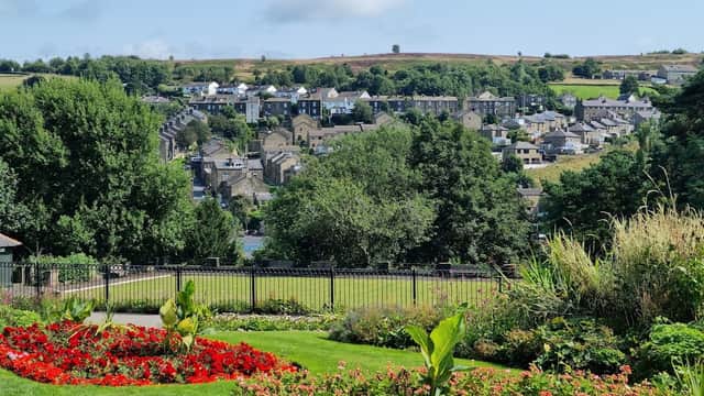 Lush green park with vibrant flowerbeds, overlooking a charming village and rolling hills under a clear blue sky.