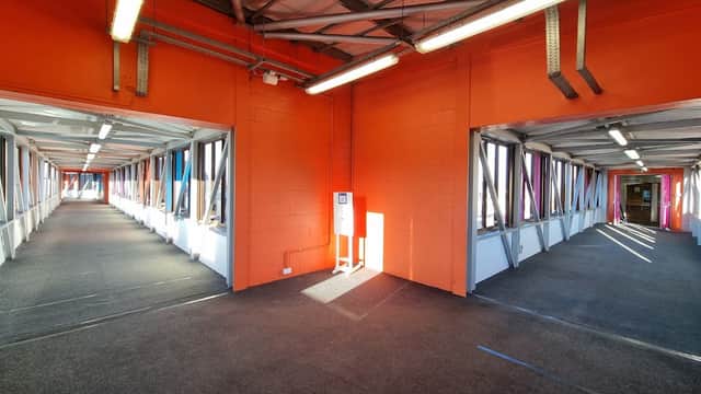 Bright orange walls and gray carpet in a multi-storey car park with open walkways and natural light streaming in.