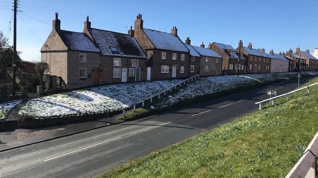Snow-covered cottages line a quiet street in Stillington, Yorkshire, under a clear blue sky.