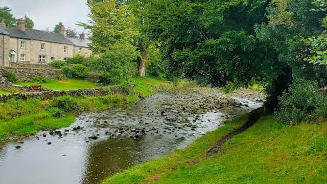 A tranquil scene by a stream, with lush greenery and a wooden bench overlooking the water near Clapham Village Hall.