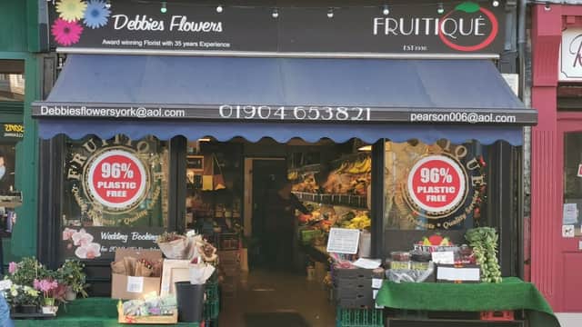 Colorful flower displays outside "Debbie's Flowers" shop, with signs promoting plastic-free products and a welcoming entrance.