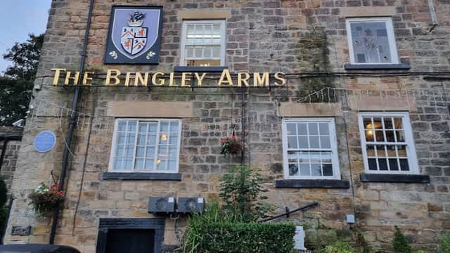 Historic stone building with "The Bingley Arms" sign, decorative plants, and blue plaque in Bardsey, Yorkshire.