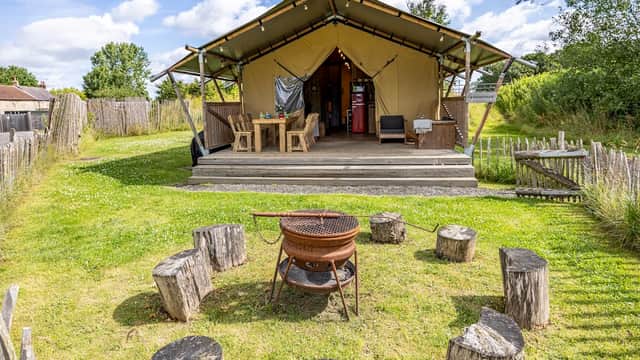 Glamping tent with wooden seating around a fire pit, surrounded by greenery and a rustic fence in Thornborough.