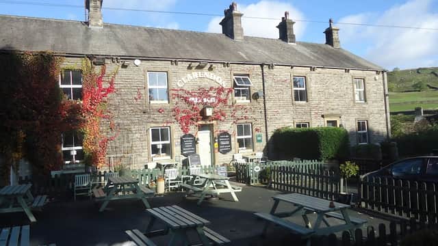 Historic stone building with ivy, outdoor seating, and a sign reading "Clarendon Hotel" against a blue sky.
