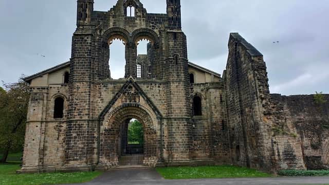 Ruins of Kirkstall Abbey with stone walls, archway, and grassy area under a cloudy sky.