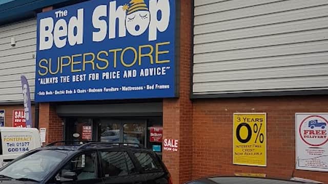 The Bed Shop Superstore storefront with blue signage, parked cars, and promotional sale signs.