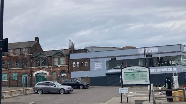 Trinity Street Car Park with parked cars, a sign reading "WELCOME TO SOUTHPAW," and industrial buildings in the background.