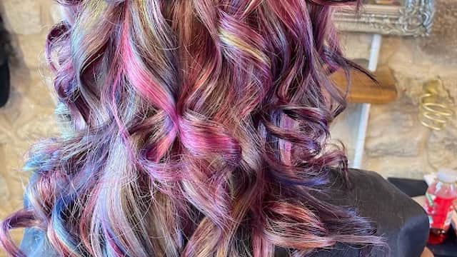 Vibrant, multi-colored curly hair styled elegantly, with a reflection of a stylist in the background.