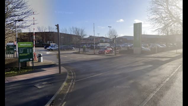 Car park entrance with signage for Waitrose, vehicles parked, and trees lining the area in York, Yorkshire.