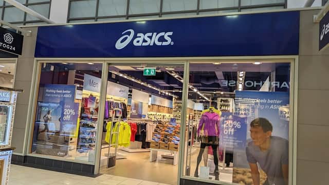 ASICS store front in a shopping center, featuring sports apparel and footwear, with promotional signage visible.