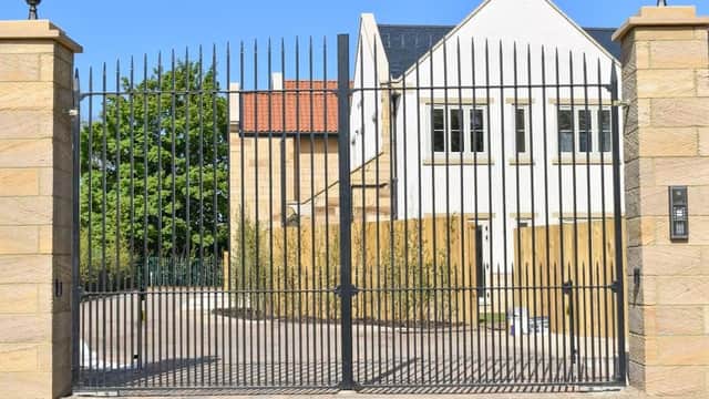 Black wrought iron gates with stone pillars, leading to a modern building with a white facade and blue roof.