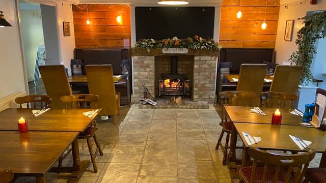 Cozy bar interior with wooden tables, chairs, a brick fireplace, and decorative plants in Welbury, Yorkshire.