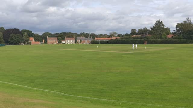 Village hall in Green Hammerton with cricket players on a lush green field under a cloudy sky.