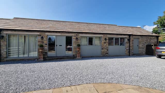 Stone building with grey doors, large windows, and a gravel driveway, surrounded by greenery in Hutton Hang, Yorkshire.