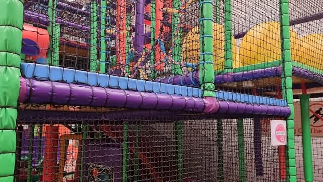 Colorful indoor play structure with nets, slides, and climbing areas for children in a vibrant setting.