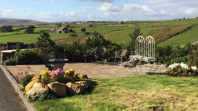 Scenic garden patio with seating, flowers, and rolling green hills under a partly cloudy sky at Leeming Wells Hotel.