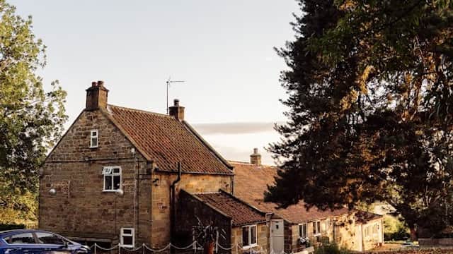 Charming stone guest house with a sloped roof, surrounded by trees and outdoor seating area in Ingleby Arncliffe, Yorkshire.