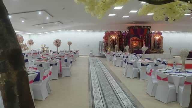 Elegant banquet hall with white tables, colorful chair covers, floral decorations, and a stage backdrop.