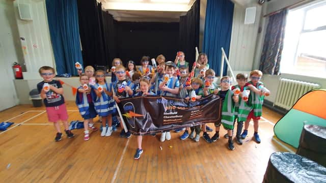 Children holding water guns and a banner inside Bardsey Village Hall, with colorful decorations and a wooden floor.