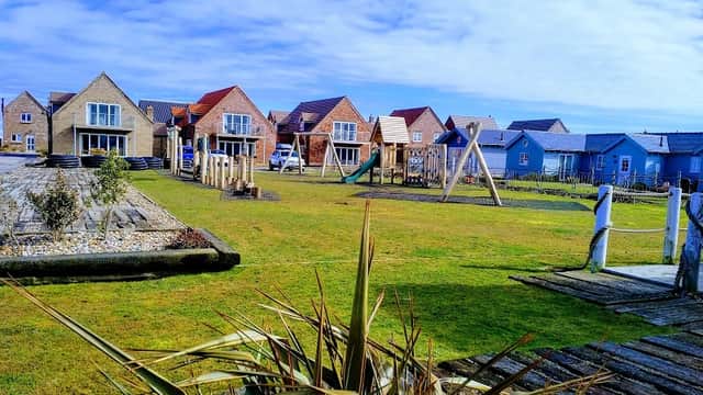 Colorful lodges with playground equipment and grassy areas under a blue sky at Puffin Lodge, Filey.