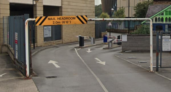 Pay & Display entrance with a height restriction sign, arrows directing traffic, and surrounding buildings in Huddersfield.