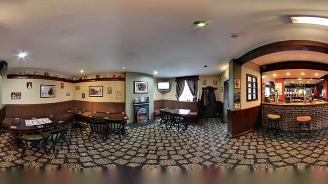 Cozy pub interior with patterned carpet, wooden tables, a bar area, and vintage decor on the walls.