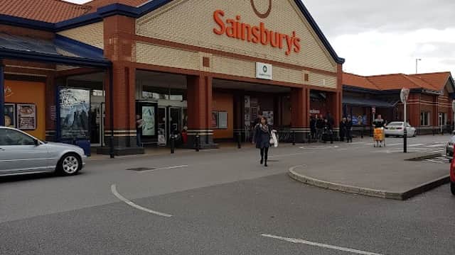 Sainsbury's storefront in Colton, Yorkshire, with shoppers and cars in the parking lot under a cloudy sky.