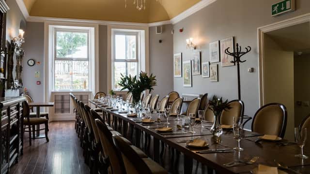 Elegant dining room with a long table set for a meal, large windows, and decorative plants in a cozy bar setting.