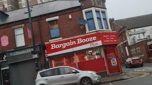 Bargain Booze Plus storefront with red signage, a gray car parked outside, and residential buildings in the background.