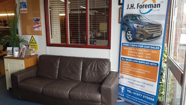 Sign for J.H. Foreman Ltd with car sales information next to a brown leather sofa in a shop interior.