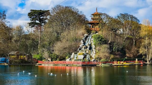 Serene lake with a waterfall, surrounded by trees and a pagoda, under a blue sky with fluffy clouds.