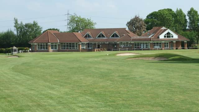 Spacious golf club building with large windows, surrounded by lush green grass and trees under a clear blue sky.