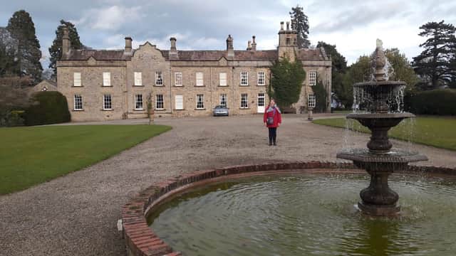 Historic Thornton Watlass Hall with a fountain in the foreground and manicured gardens, set against a cloudy sky.