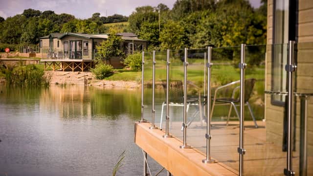 Lakeside view at Wayside Holiday Park with modern lodges and glass railings, surrounded by greenery in Yorkshire.