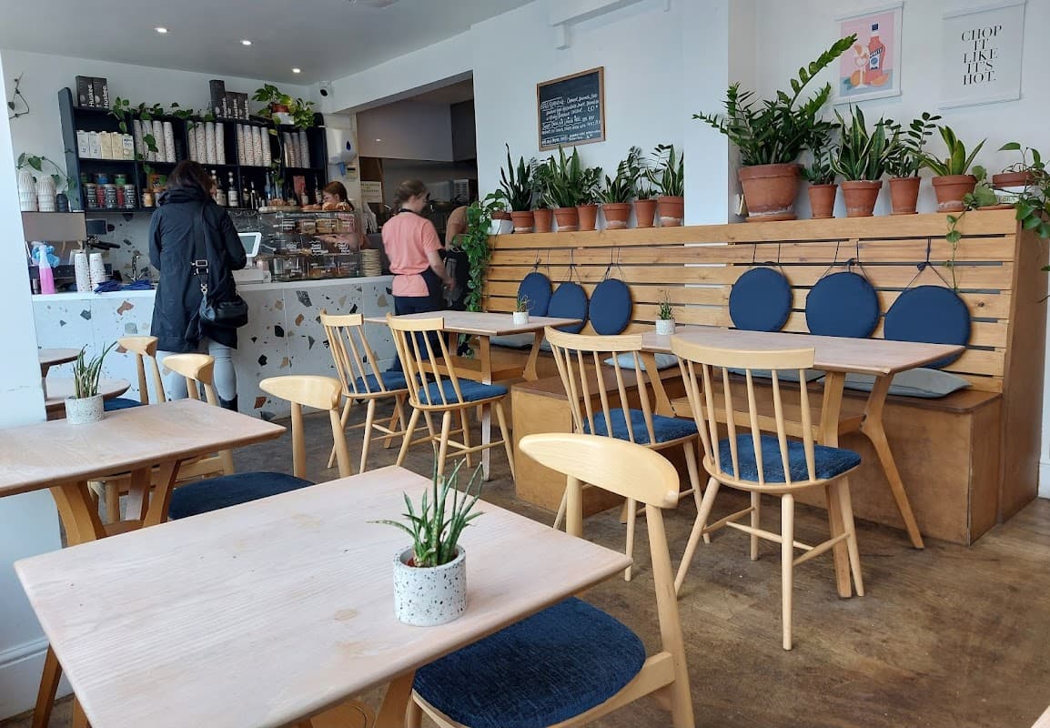 Cozy café interior with wooden tables, blue cushions, plants, and a counter displaying baked goods.