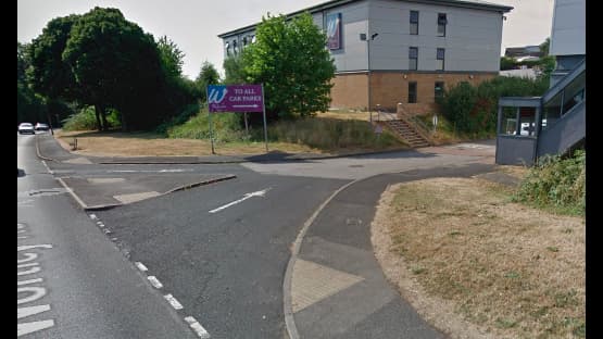 Pay & Display sign for "YourParkingSpace" near a road, with grassy areas and a building in the background.