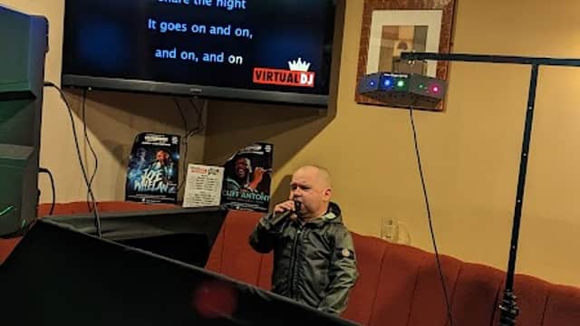 A small stage with a microphone, a karaoke screen displaying lyrics, and colorful lights in a lively atmosphere.