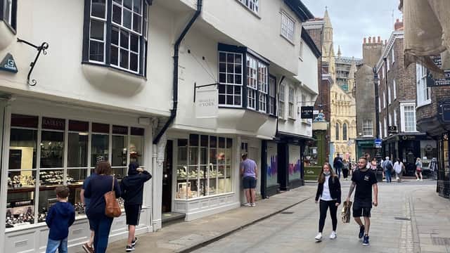 Bradleys The Jewellers storefront with display cases, people walking on a cobblestone street, and York Minster in the background.