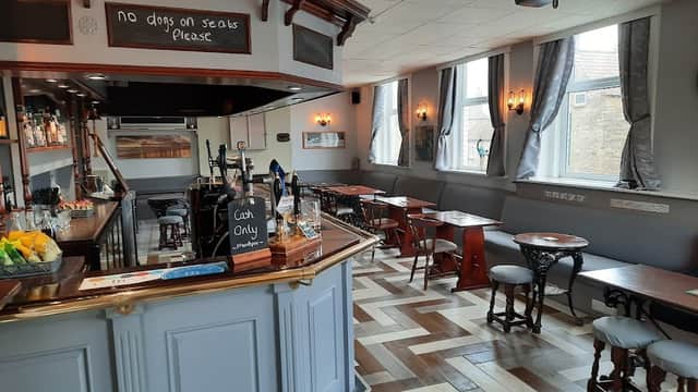 Cozy bar interior with wooden furniture, a polished counter, and large windows, featuring a no dogs sign.