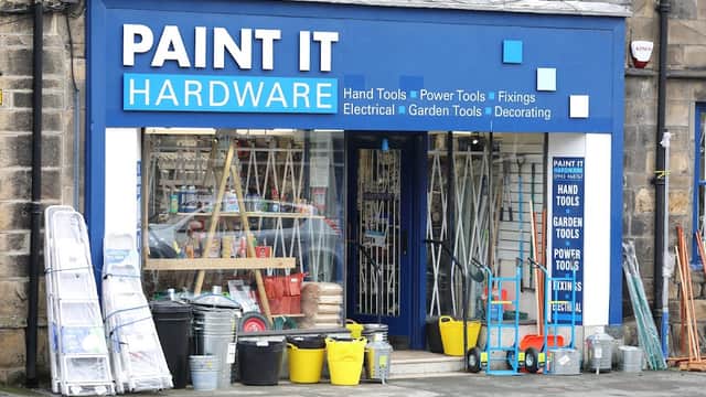Bright blue storefront with "Paint It Hardware" sign, displaying tools, paint supplies, and garden equipment outside.