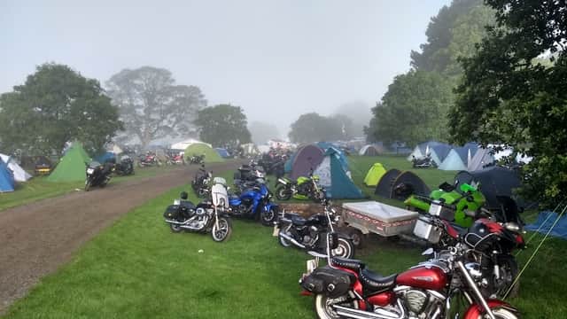 Tents and motorcycles scattered across a grassy field, surrounded by misty trees in a serene outdoor setting.